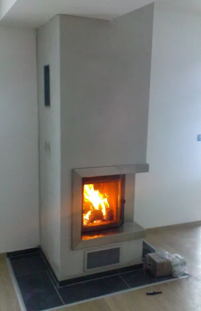 Bíle omítnutý krb s&nbsp;krbovou vložkou a&nbsp;hořícím ohněm