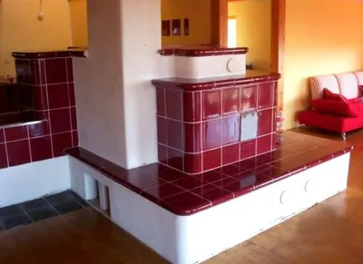 Vínově červená kachlová kamna s&nbsp;bílým soklem v&nbsp;obývacím pokoji