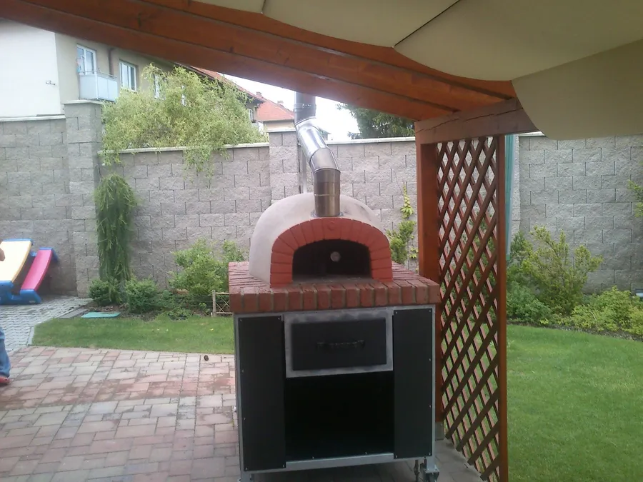 Kupolová pec na pizzu s&nbsp;cihlovým ústím a&nbsp;nerezovým komínem pod dřevěnou pergolou